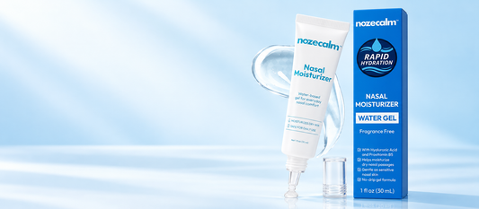Illustrative studio scene of NozeCalm nasal moisturizer tube and blue carton, with its clear tapered applicator, on a pale blue background