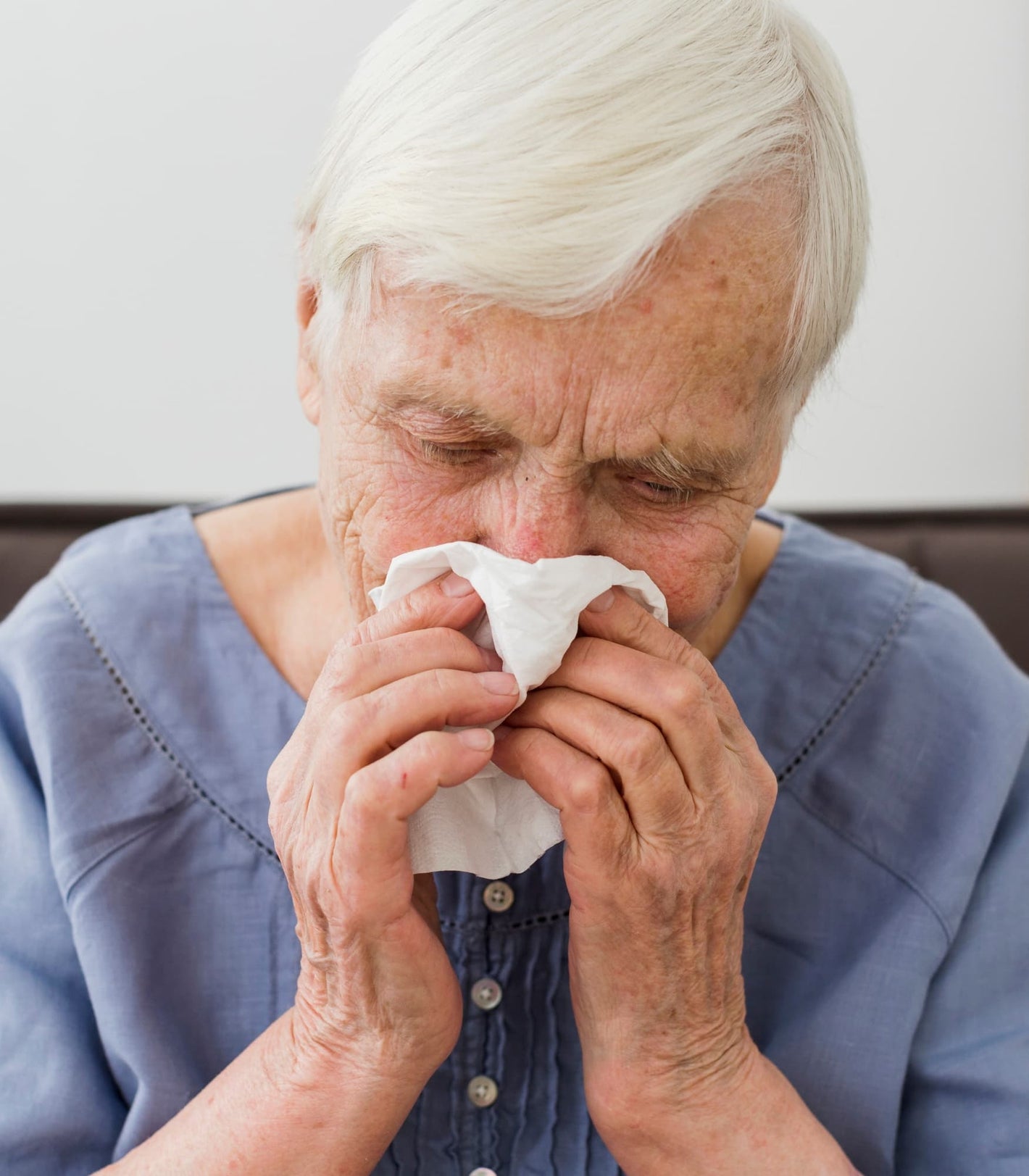 A senior woman using a tissue for a nosebleed, for whom NozeCalm provides gentle care.