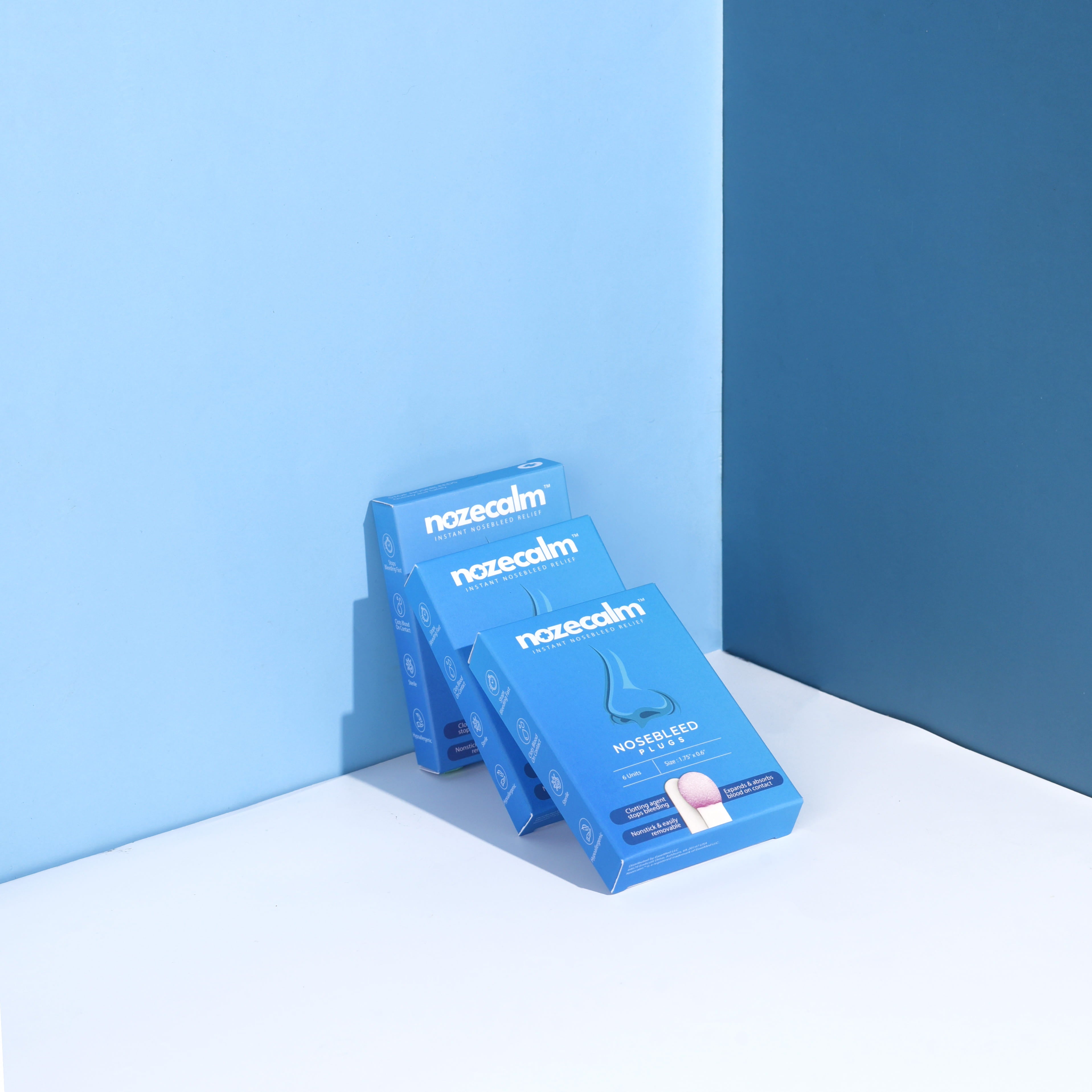 Three boxes of NozeCalm nosebleed plugs arranged in a professional product shot.